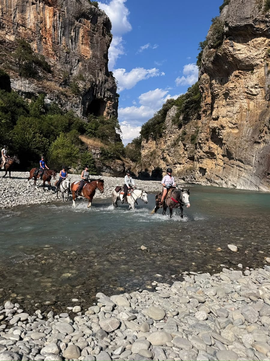 A horseback riding group crossing a shallow river near a canyon