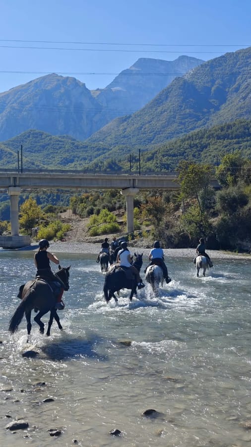 Riders crossing the river under a bridge in the Vjosa valley