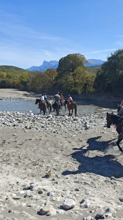 Riders crossing a stony river bed below mountains